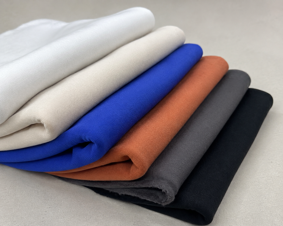 Fabric Lot AI-restaged source range photograph: six smooth knit fabric faces in white, cream, blue, terracotta, gray and black.